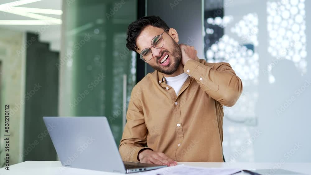 Tired businessman suffering from neck pain while working on laptop while sitting at desk at workplace in business office. Upset man worker in glasses massages and rubs sore muscles, stretches Tired businessman suffering from neck pain while working on laptop while sitting at desk at workplace in business office. Upset man worker in glasses massages and rubs sore muscles, stretches