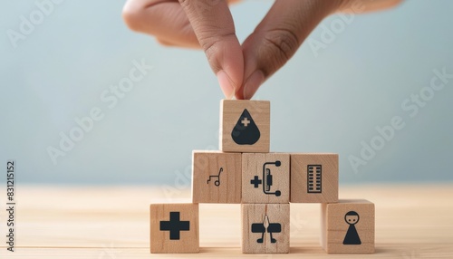 The photo shows a hand placing a wooden block with a water drop icon on top of a stack of other wooden blocks