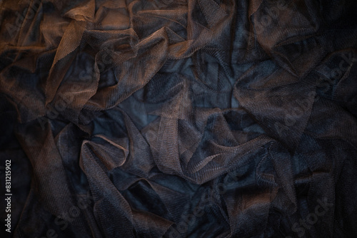Black translucent fabric is draped and textured with numerous folds and creases, highlighted by soft, dim lighting. photo