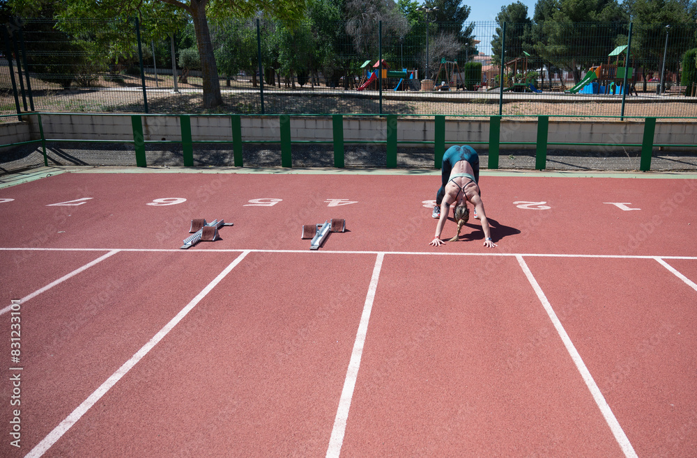Fototapeta premium Female athlete in downward dog pose on running track
