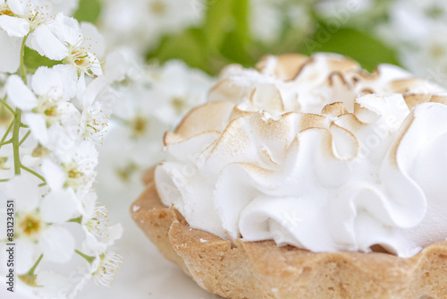Delicious tartlet with meringue on a white floral background. Sweet treat in spring or summer