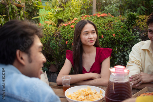 A young timid asian woman listening to an interesting conversation with her friends during an outdoor picnic in a lush garden or lawn.