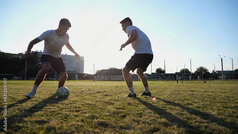 Two sportsmen playing in soccer in stadium at sunset. Professional footballers performing tricks with ball at green field. Young men training at meadow. Concept of a freestyle football. Slow motion Two sportsmen playing in soccer in stadium at sunset. Professional footballers performing tricks with ball at green field. Young men training at meadow. Concept of a freestyle football. Slow motion