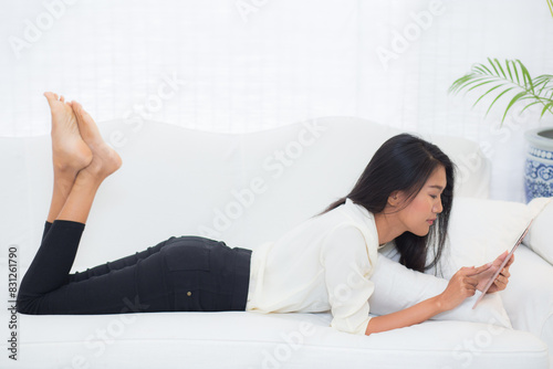 Beautiful portrait young asian woman smile and happy using digital tablet computer with lying couch at home, girl with satisfy social internet online, business communication concept.