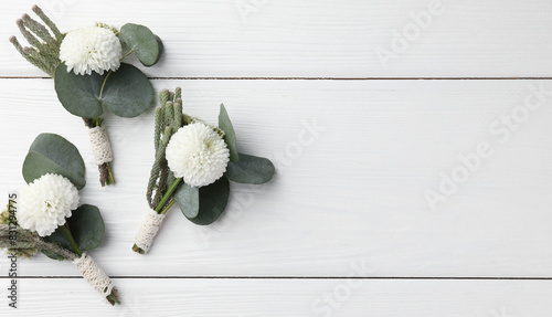 Small stylish boutonnieres on white wooden table, flat lay. Space for text photo