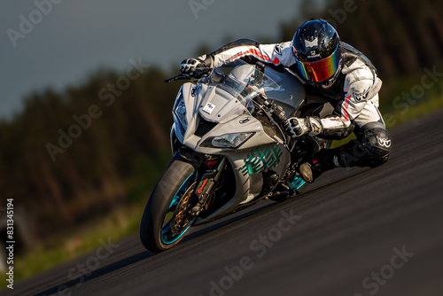  A man rides a white motorcycle on the race track  surrounded by trees in the background and a expansive sky above