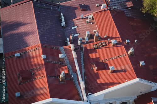 Pipes of the ventilation system on the red roof of a restaurant in an ancient building. Top view on a summer evening. Air conditioners, wooden stairs and windows are located randomly and chaotically.