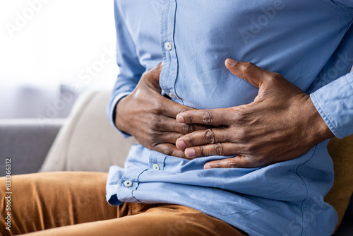фотографія A man is shown clutching his stomach in pain, experiencing abdominal discomfort suggesting gastrointestinal health issues or illness
