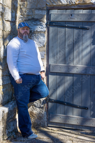 Man with plaid cap and beard poses by rustic exterior building. photo