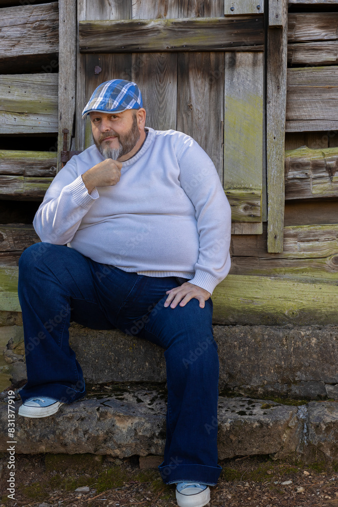 Man with plaid cap and beard poses by rustic exterior building. Man with plaid cap and beard poses by rustic exterior building.
