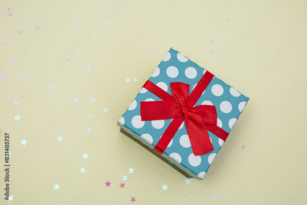 Gift box decorated with bright red knotted bow and dotted wrapping paper, ribbon, glitter decorative stars. Present, celebration, anniversary concept composition. Gift box decorated with bright red knotted bow and dotted wrapping paper, ribbon, glitter decorative stars. Present, celebration, anniversary concept composition.