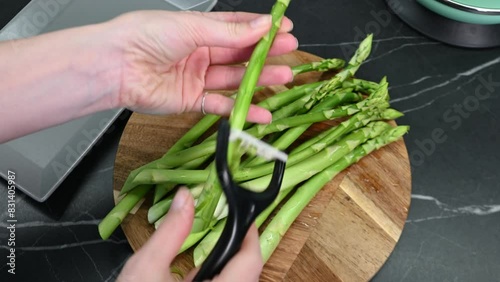 Girl hands peel the green asparagus - clean peel vegetable. Woman peeling the edible sprouts of asparagus with a vegetable peeler.
