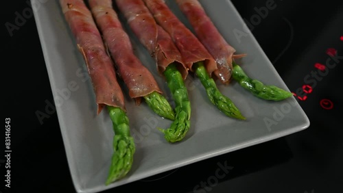 freshly cooked asparagus wrapped with bacon on ceramic plate