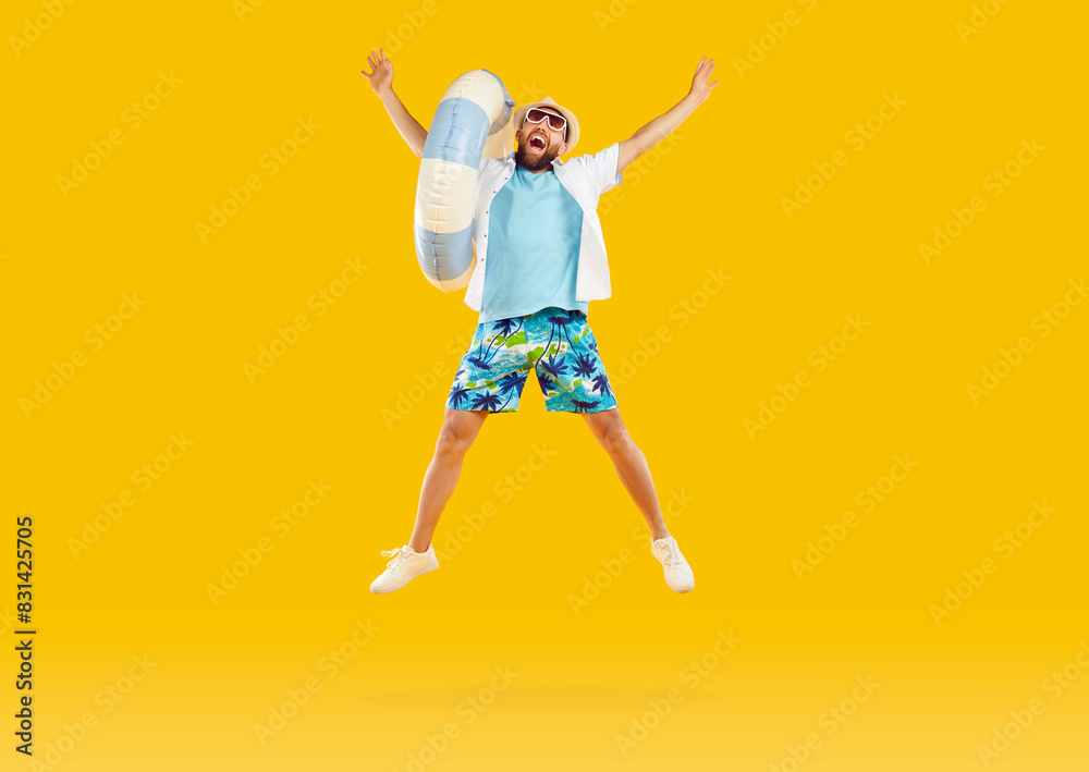 Cheerful male vacationer with inflatable beach circle jumping high on orange studio background. Funny young man in summer shorts, t-shirt, panama and sunglasses. Summer, vacation and people concept Cheerful male vacationer with inflatable beach circle jumping high on orange studio background. Funny young man in summer shorts, t-shirt, panama and sunglasses. Summer, vacation and people concept