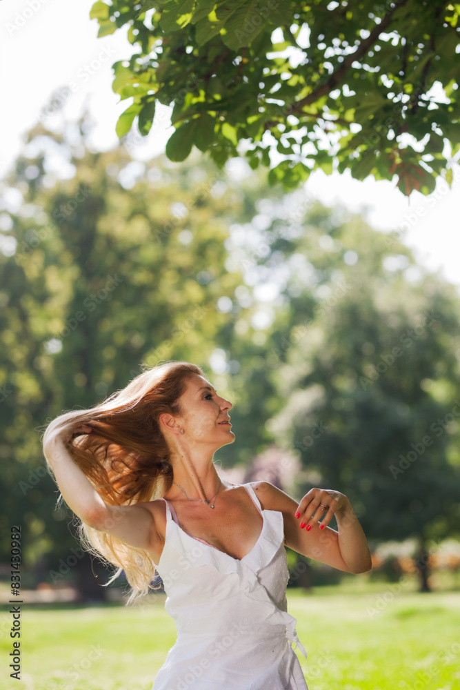 Obraz premium A carefree young woman with long hair experiences the joy of a sunny day in a lush green park, embracing a gentle summer breeze.