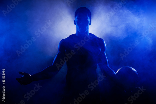 Basketball player holding a ball against blue fog background. Muscular african american man silhouette. © Nikola Spasenoski