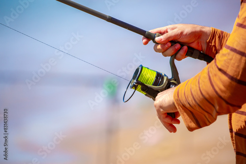 Fisherman's hands turning a reel on a fishing rod. Close-up of fishing reels. Fishing on the shore of the lake. Spinning rods for sport fishing. photo
