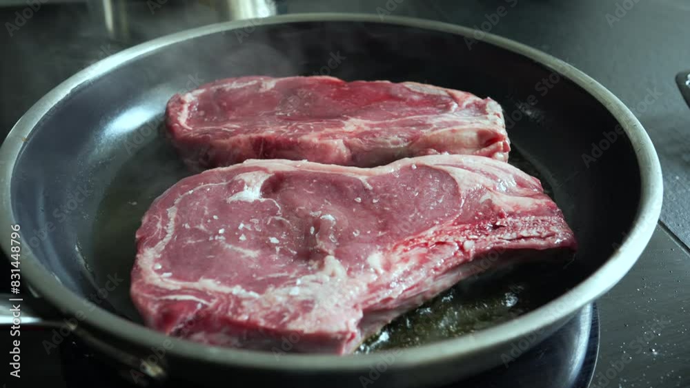 Raw steaks sizzling in a hot pan, lightly salted, beginning to cook, close-up view of fresh beef, home cooking process, preparing a delicious meal, culinary detail, kitchen scene Raw steaks sizzling in a hot pan, lightly salted, beginning to cook, close-up view of fresh beef, home cooking process, preparing a delicious meal, culinary detail, kitchen scene