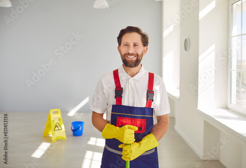 Janitor from cleaning service at work. Cleaning company worker helps keep indoor space clean and sanitary. Happy man in workwear standing inside building, holding mop, looking at camera and smiling © Studio Romantic