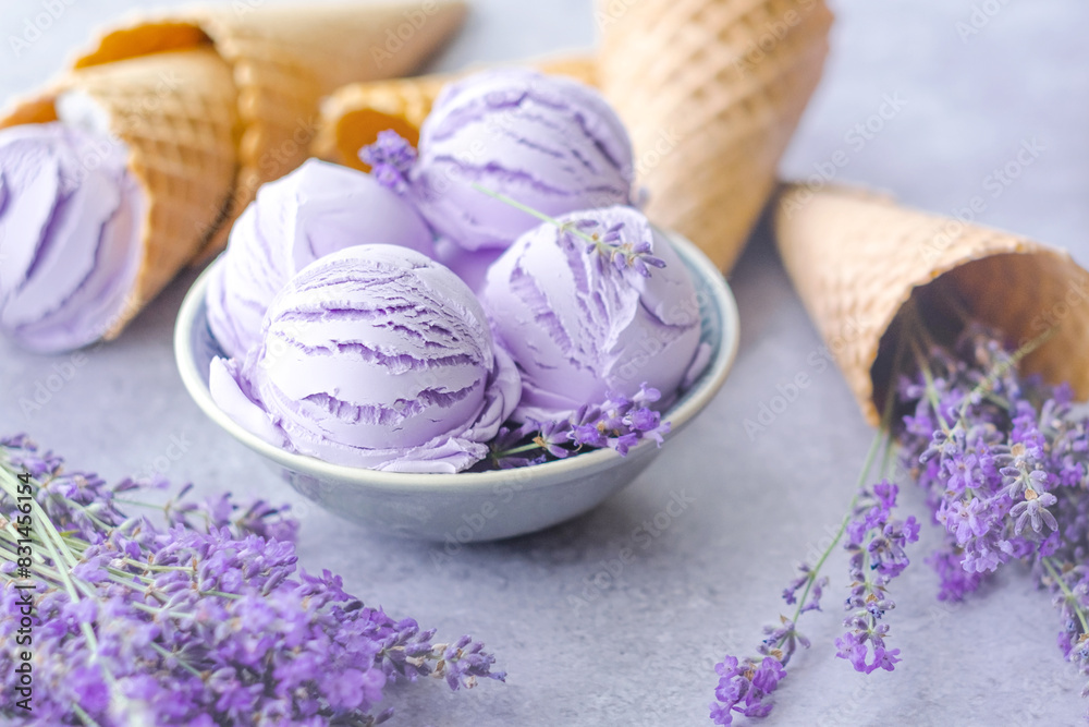 Close up creamy lavender ice cream balls in a bowl with lavender flowers, waffle cones on a gray background. Summer healthy dessert. Mental health and reduce stress Close up creamy lavender ice cream balls in a bowl with lavender flowers, waffle cones on a gray background. Summer healthy dessert. Mental health and reduce stress
