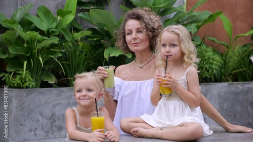 Mom and twins smile and enjoy drinking freshly squeezed juice and smoothies through straws. Family happily drinks cool drinks on hot summer day Happy kids drink natural and healthy juices with delight