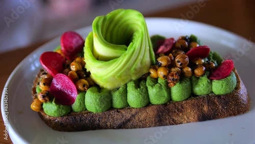 On plate is healthy snack - toast, decorated with avocado, vegetables and legumes. Healthy toast is choice for those who prefer nutritious food. Healthy snack delight with variety flavors and textures