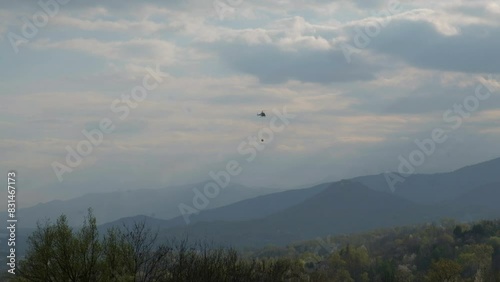 A helicopter fighting a fire carries a bucket of water to drop on a wildfire burning out of control at a brush fire. photo