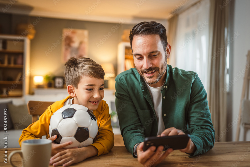 Father and son watch football match on mobile phone and cheer at home