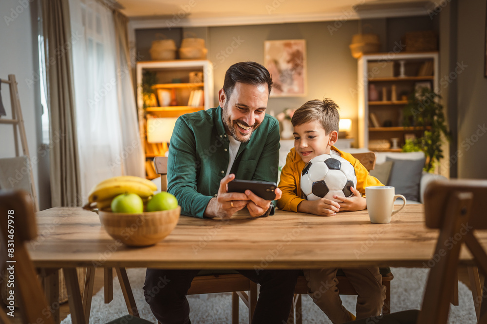 Fototapeta premium Father and son watch football match on mobile phone and cheer at home