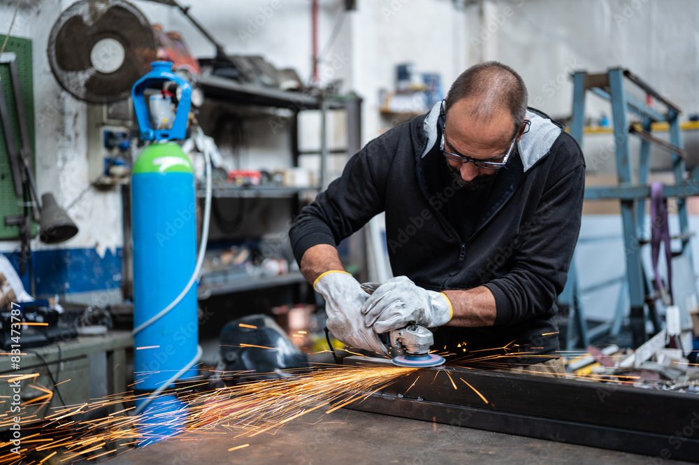 Using the flexible disc grinder on a metal bar: When the tool touches the surface, numerous orange sparks are projected. Concept of metal processing in the workshop, craft work. Using the flexible disc grinder on a metal bar: When the tool touches the surface, numerous orange sparks are projected. Concept of metal processing in the workshop, craft work.