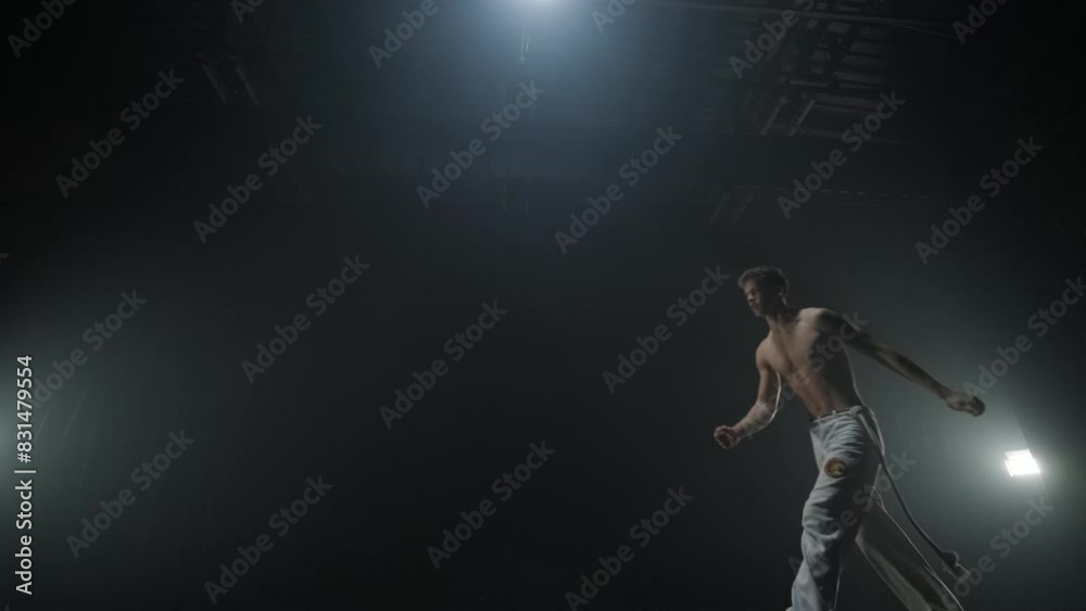 Group of a professional dancers are practicing capoeira in darkness against a spotlight on a black background of studio. Afro-Brazilian martial art that combine elements of dance. Group of a professional dancers are practicing capoeira in darkness against a spotlight on a black background of studio. Afro-Brazilian martial art that combine elements of dance.