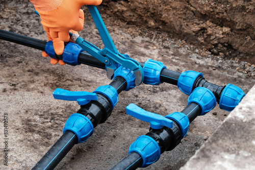 Plumber using a wrench tightens a compression fitting onto a HDPE pipe with a tap, installing a water supply system for automatic watering