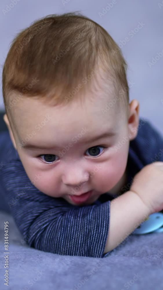Lovely toddler in blue clothes lying peacefully on the bed. Cute child looks at pacifier with interest and then around himself. Vertical video Lovely toddler in blue clothes lying peacefully on the bed. Cute child looks at pacifier with interest and then around himself. Vertical video