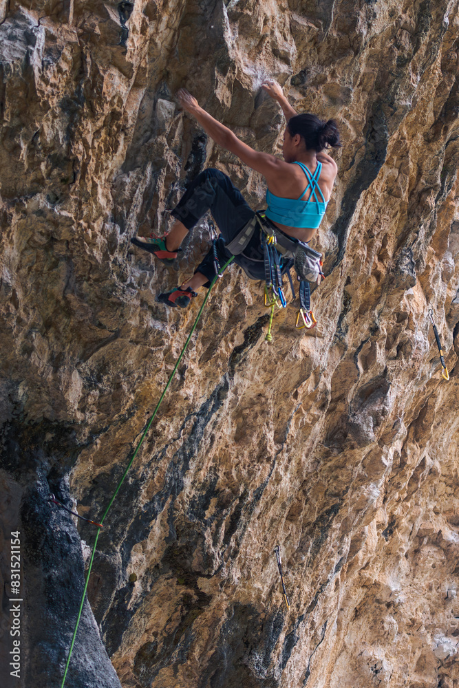 Obraz premium A woman is climbing a rock wall with a green rope. Vertical.