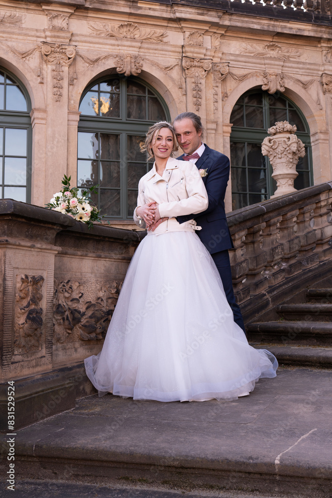 Fototapeta premium Beautiful couple, newlyweds on a walk. Bride and groom are standing on steps of the palace. Family
