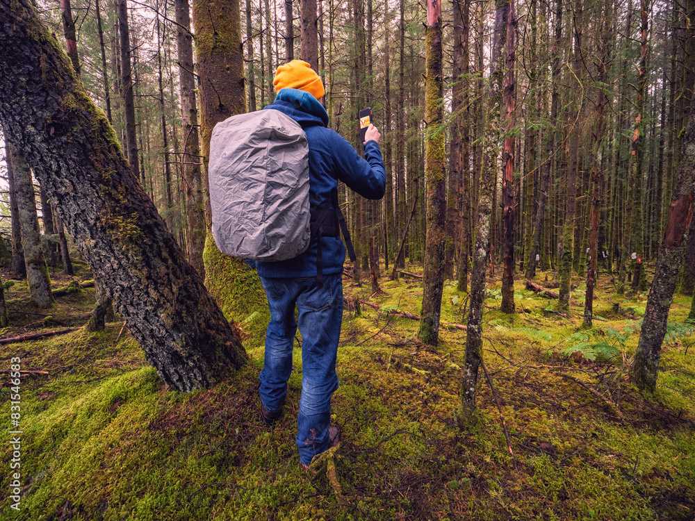 A man is walking through a forest with a backpack on his back. He is taking a picture with his cell phone. Scene is peaceful and serene, as the man is surrounded by nature. Travel and tourism theme A man is walking through a forest with a backpack on his back. He is taking a picture with his cell phone. Scene is peaceful and serene, as the man is surrounded by nature. Travel and tourism theme