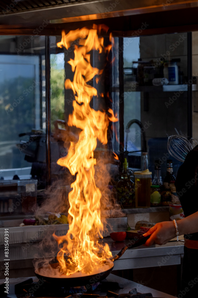 Chef creates flame in pan. Chef cooking with flame in a frying pan on a kitchen stove. Young chef in the restaurant kitchen making flambe in the frying. Chef creates flame in pan. Chef cooking with flame in a frying pan on a kitchen stove. Young chef in the restaurant kitchen making flambe in the frying.