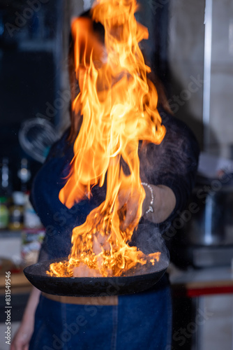 Chef creates flame in pan. Chef cooking with flame in a frying pan on a kitchen stove. Young chef in the restaurant kitchen making flambe in the frying.