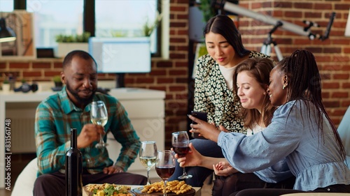 Fotografía Multiracial friends at apartment party looking at social media posts made by acquaintance on cellphone, making fun of them