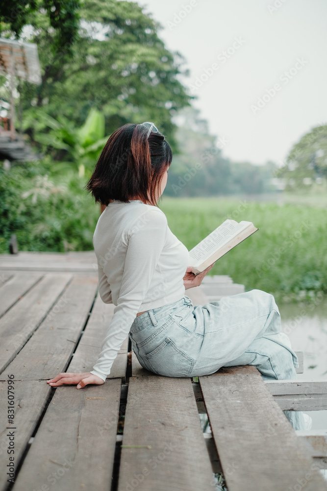 A woman is sitting on a wooden pier reading a book. The scene is peaceful and serene, with the woman enjoying her time alone A woman is sitting on a wooden pier reading a book. The scene is peaceful and serene, with the woman enjoying her time alone