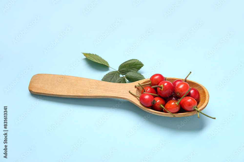 Wooden spoon with fresh rose hip berries and leaves on blue background Wooden spoon with fresh rose hip berries and leaves on blue background