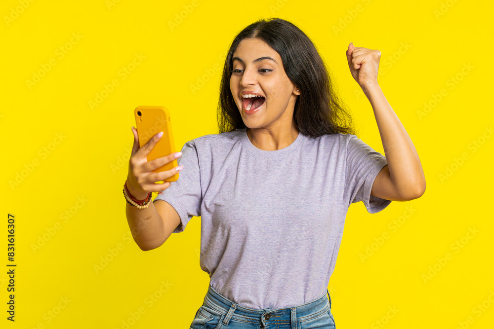 Happy excited Indian woman girl use smartphone typing browsing screaming say wow yes found out great win good news lottery goal achievement celebrating success, winning play game on yellow background Happy excited Indian woman girl use smartphone typing browsing screaming say wow yes found out great win good news lottery goal achievement celebrating success, winning play game on yellow background
