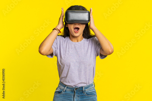 Excited happy Indian young woman using headset helmet app to play simulation game. Watching virtual reality 3D 360 video. Arabian girl in VR goggles isolated on yellow background. Future technology © Andrii Iemelianenko