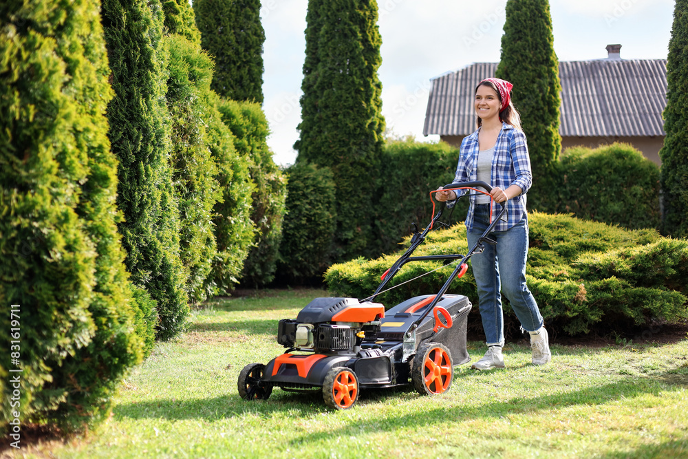 Smiling woman cutting green grass with lawn mower in garden Smiling woman cutting green grass with lawn mower in garden