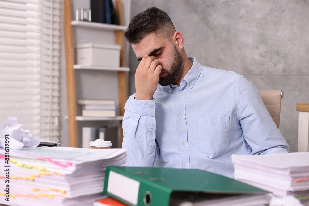 Overwhelmed man surrounded by documents at workplace in office Overwhelmed man surrounded by documents at workplace in office