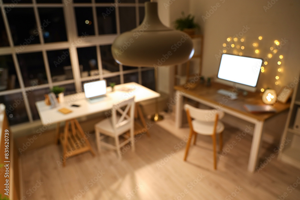 Fototapeta premium Blurred view of office with desks and glowing lights at night