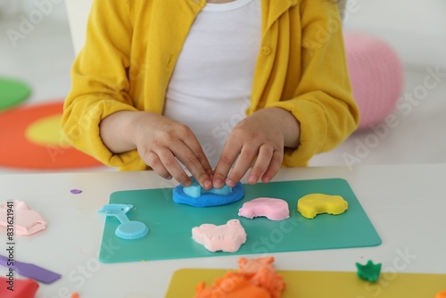 Little girl sculpting with play dough at table indoors, closeup