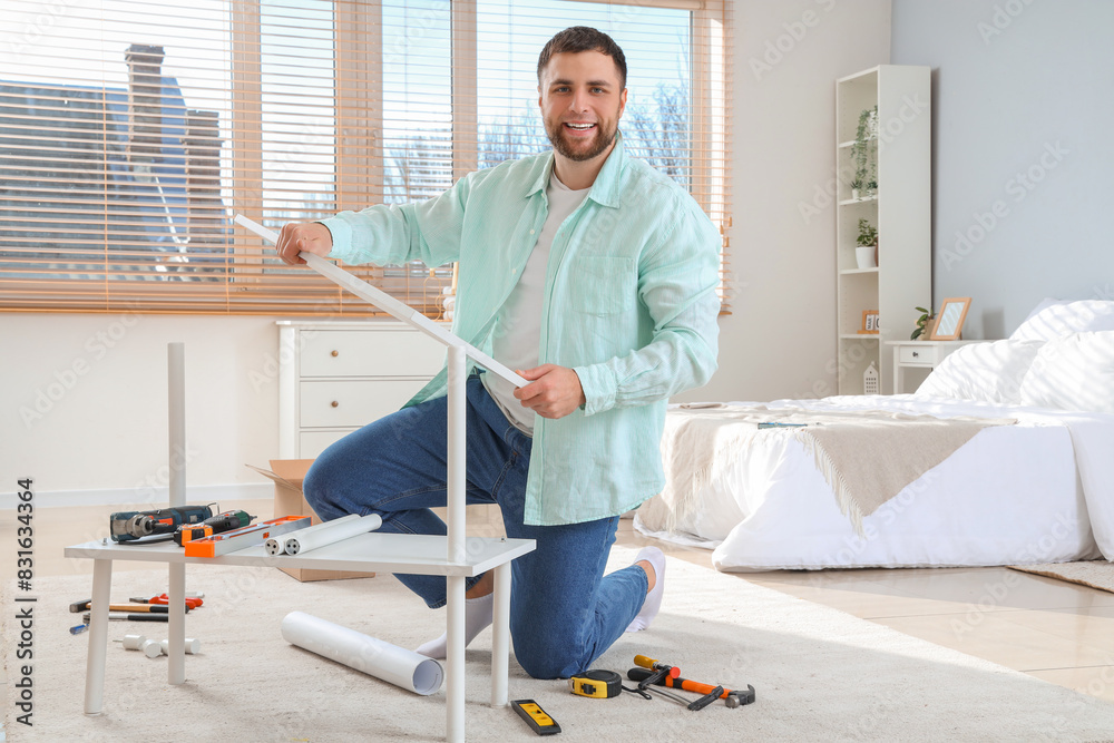 Young man assembling white shelf unit in bedroom