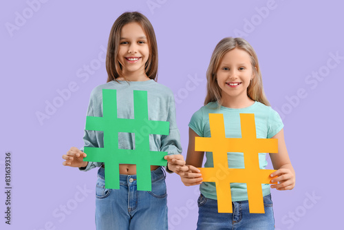 Cute teenage girls with hashtags on lilac background photo