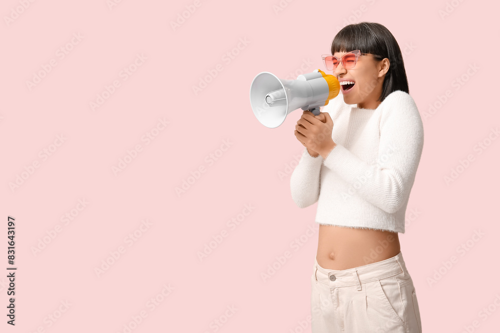 Screaming young woman with megaphone  on pink background